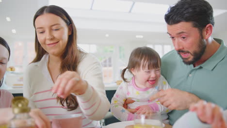 Familia-Con-Hija-Con-Síndrome-De-Down-Sentada-Alrededor-De-Una-Mesa-En-Casa-Desayunando