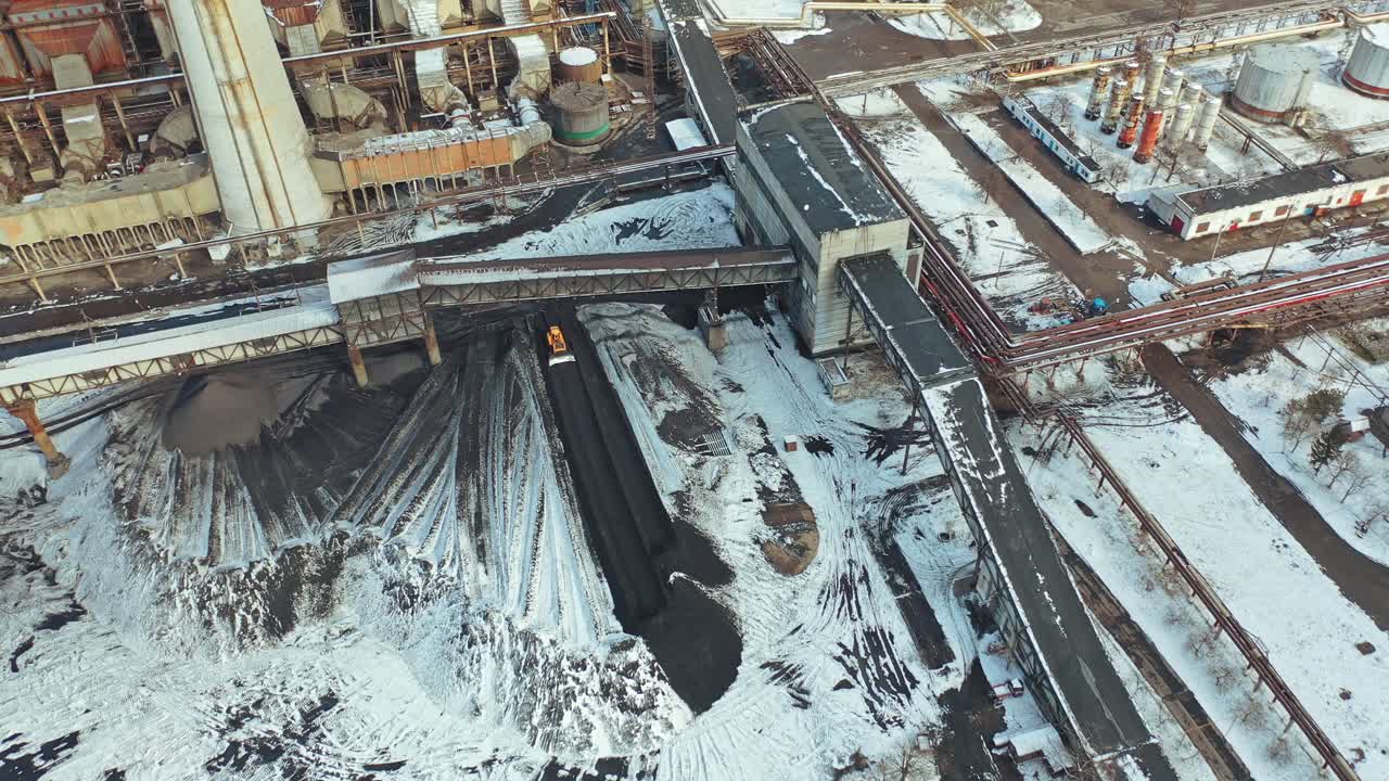 Yellow excavator smoothes black ash from coal under the bridge in the territory of the heating power station. Aerial view.