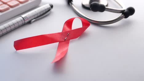 red ribbon on a desk with medical supplies: aids awareness