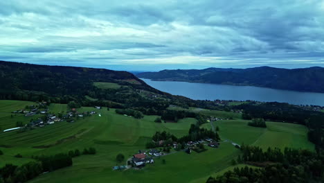 village in green fields on shore of mountain lake below cloudy sky