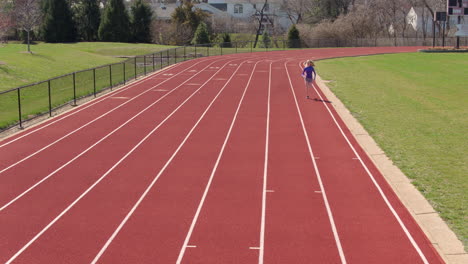 teen girl on a track breaks into a run towards and past camera on a pretty day