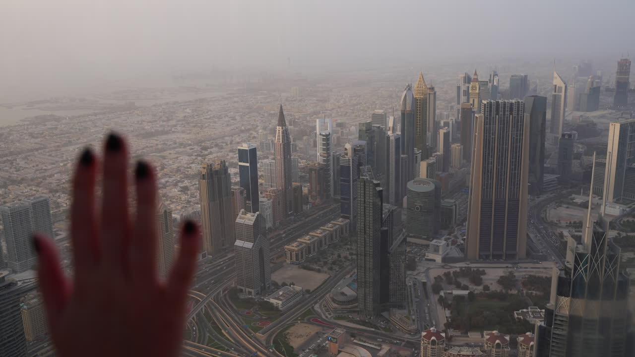 Skyline di Dubai dal Burj Khalifa, ragazza con la mano appoggiata sul vetro.