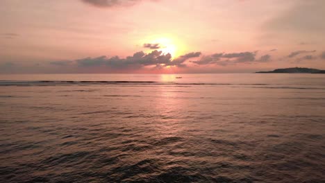 Aerial-drone-low-fly-over-ocean-towards-sun-during-bright-cloudy-sunset-on-tropical-island-bali