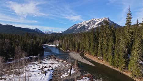 scenic ascending shot of evergreen forest, river, and snow capped mountain in background in cle elum on a blue sky day in washington state