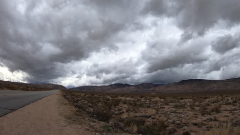 time lapse, dark storm clouds rolling over mojave desert mountains by road