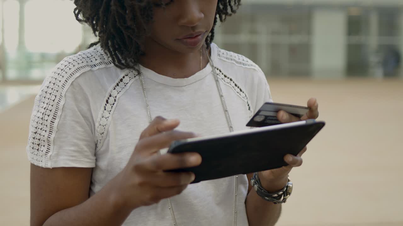 Focused African American woman typing card number on tablet.