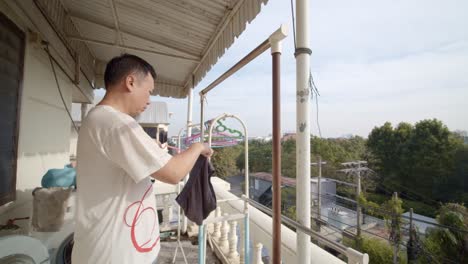 asian man hanging up clothing to dry on his apartment balcony - slow motion