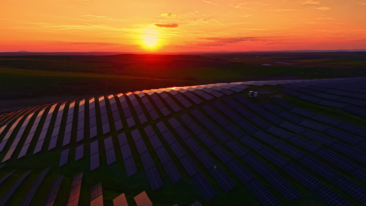 Solnedgang over solpaneler på en bred mark, der fanger dagens sidste lys nær et landområde, som leverer vedvarende energi