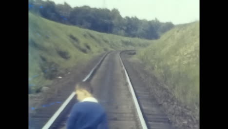 boy standing next to train track on side of road in soviet union. circa ussr 1980s: a boy stands on the side of a road next to a train track in the soviet union.