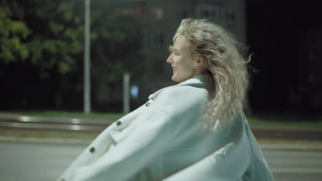 white girl exuding pure happiness as bright street light illuminates her smiling face while blurred residential building across road creates vibrant urban nighttime backdrop