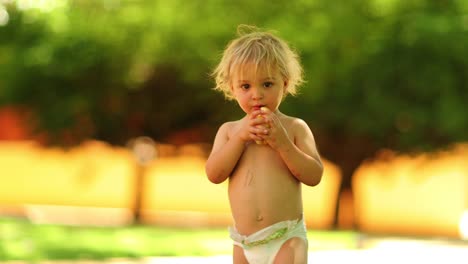 fotografía sincera de un niño pequeño rubio con pañales al aire libre en resolución de 4k. niño pequeño con una fruta de pera afuera