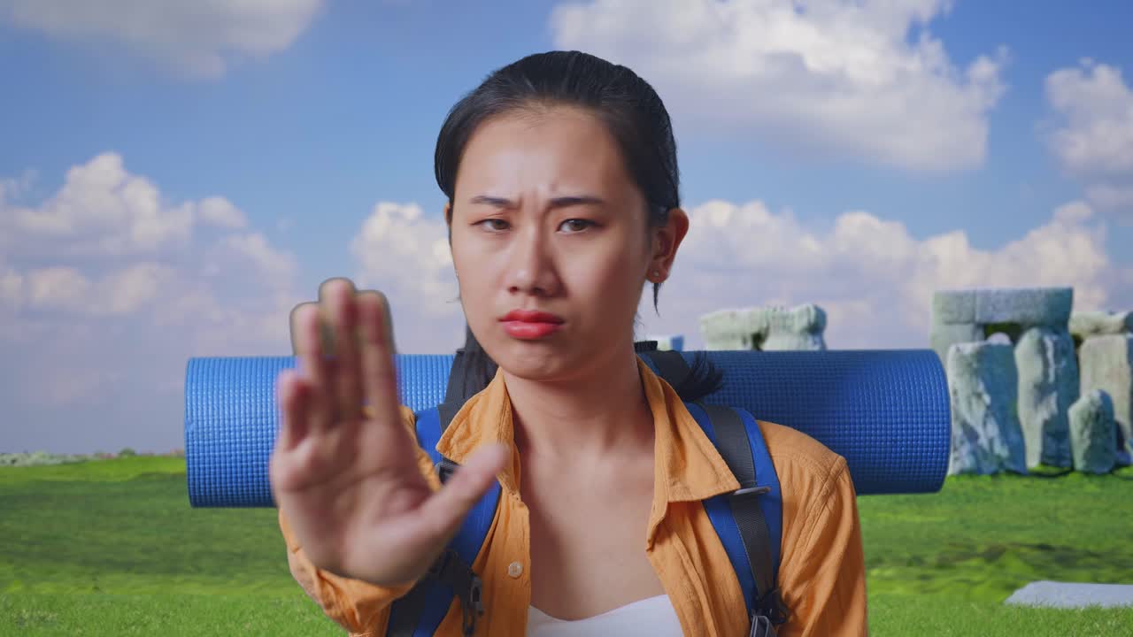 Close Up Of Asian Female Hiker With Mountaineering Backpack Looking At Camera And Making Stop Hand Sign While Traveling In Stonehenge