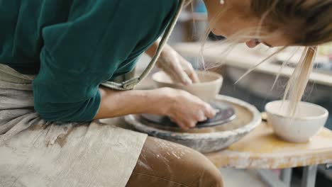 zoom out shot of woman potter making ceramic crockery on pottery wheel, slow motion