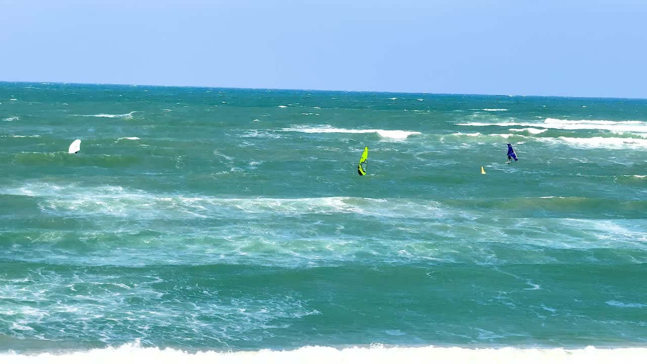 Windsurfers skillfully maneuver through ocean waves under clear skies at Torquay, Victoria. Dynamic movement captured with vibrant colors and natural lighting
