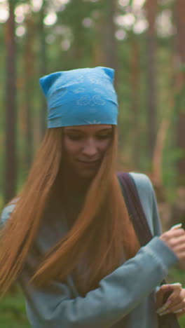 la dama de bandana azul deja caer su bolsa juguetónmente en el suelo del bosque cubierto de hierba mientras está de pie cerca de un compañero que sostiene una bolsa roja, rodeada de árboles altos y vegetación exuberante