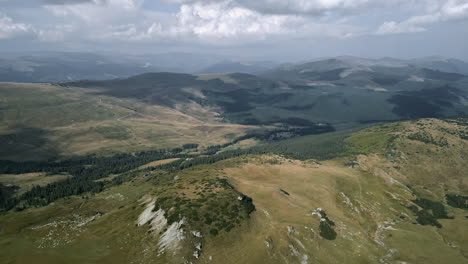 Impresionante-Vista-Aérea-De-La-Transalpina-De-Rumania,-Que-Muestra-Exuberantes-Praderas,-Densos-Bosques-De-Coníferas-Y-Terrenos-Escarpados-Bajo-Un-Cielo-Nublado,-Enfatizando-La-Grandeza-De-La-Naturaleza.