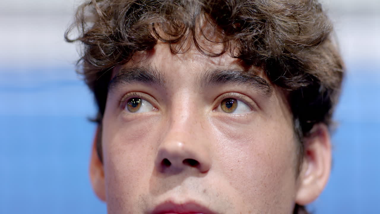 Playing padel tennis match, young man with curly hair concentrating intensely, on indoor court