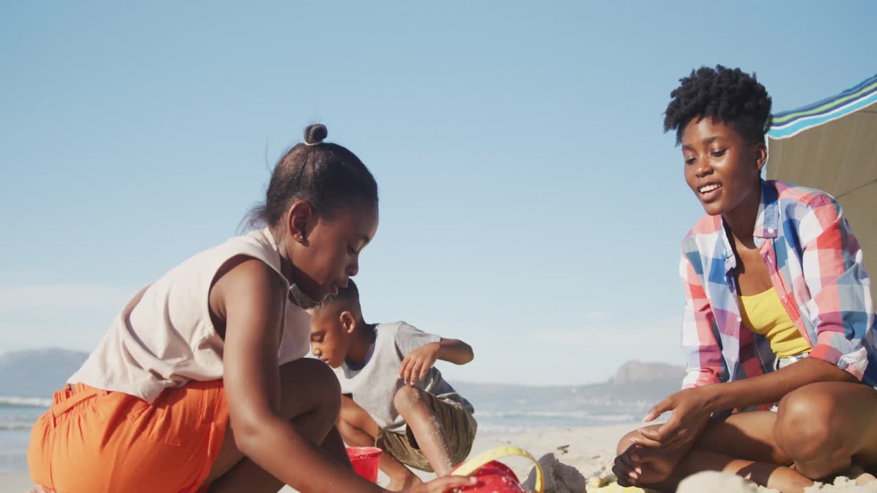 아프리카계 미국인 어머니, 딸과 아들이 해변의 모래에서 놀고 있습니다.