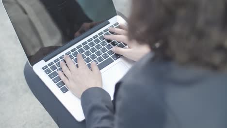 cropped shot of hands of businesswoman sitting outside and typing on laptop computer, then making winner gesture