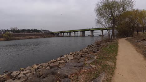 yanghwa hangang riverside park on a gloomy day - walking in the riverside path with bridge in the background. - pov, handheld shot