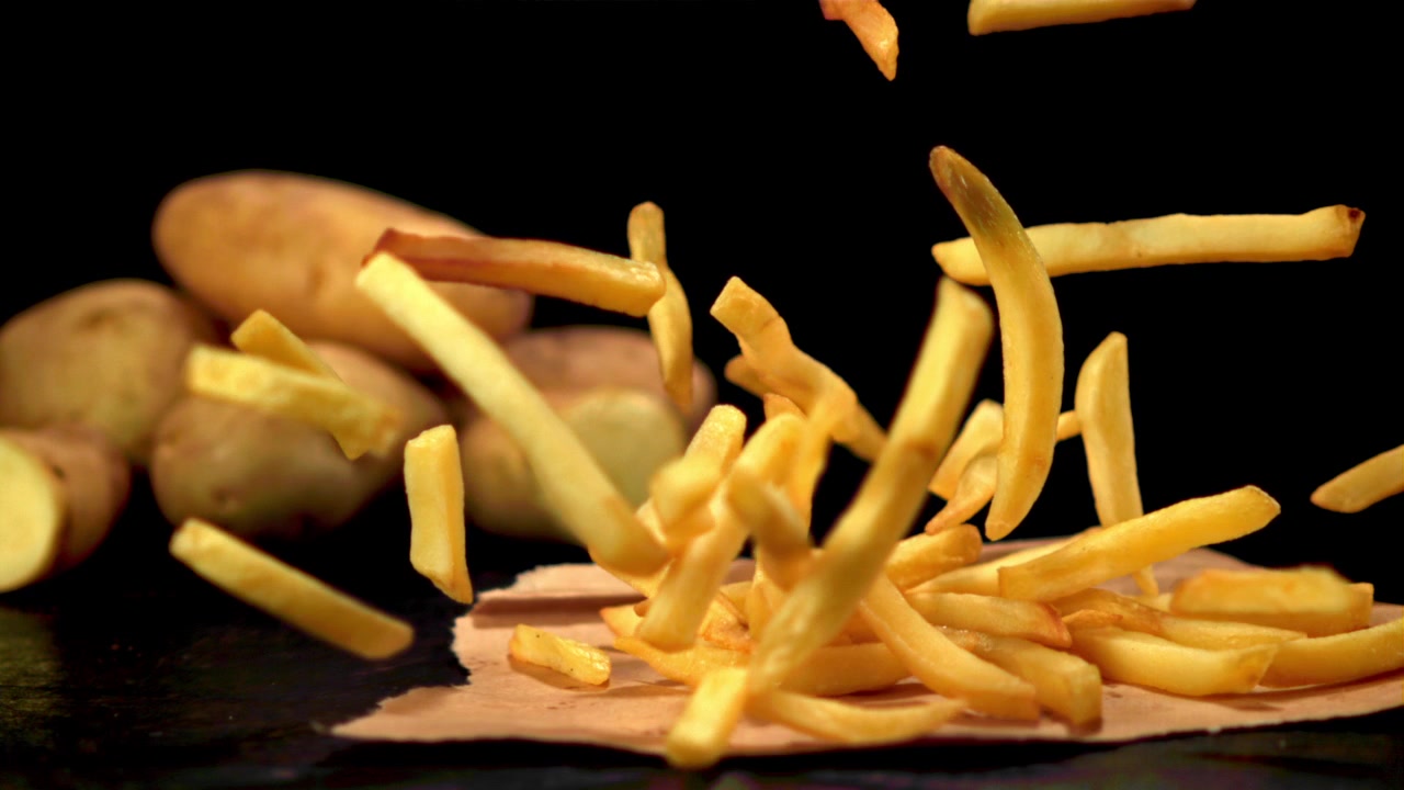 Crispy French Fries Falling with Raw Potatoes on Black Background