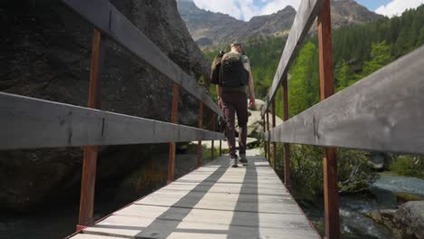 Rückansicht-Aus-Niedrigem-Winkel-Eines-Männlichen-Wanderers,-Der-Eine-Holzbrücke-Im-Gebirge-überquert