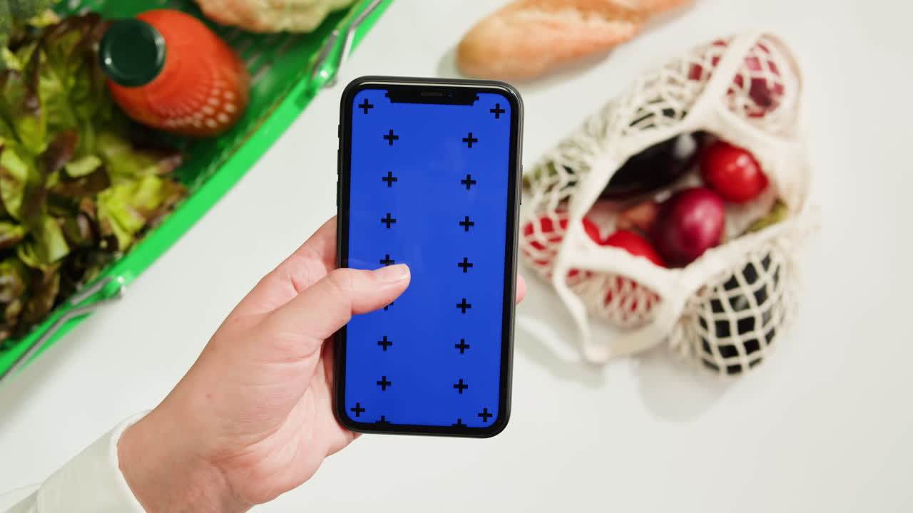 Person holding a phone with a blue screen in front of groceries