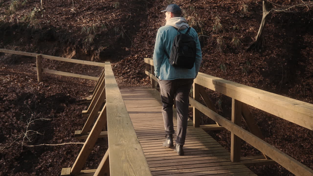 Young caucasian male adventurer crossing a wooden bridge over a canyon in a forest. Beautiful day in autumn. 4K Nature Outdoors Europe