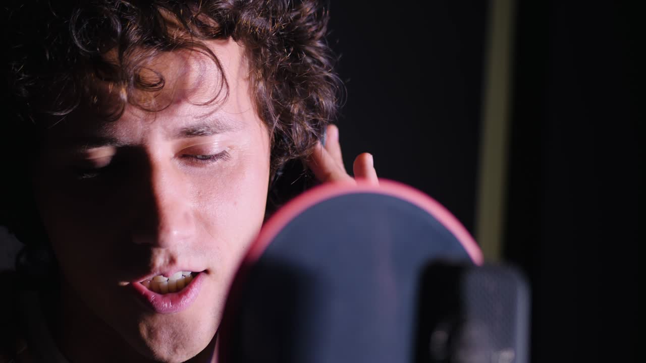 joven cantante guapo hombre emocionalmente escribiendo una canción en el estudio. grabando una nueva melodía o álbum. artista vocal masculino con cabello rizado cantando solo. cámara lenta. 4k