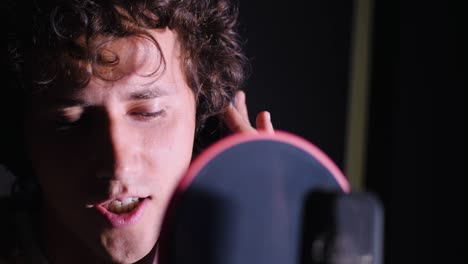 joven cantante guapo hombre emocionalmente escribiendo una canción en el estudio. grabando una nueva melodía o álbum. artista vocal masculino con cabello rizado cantando solo. cámara lenta. 4k