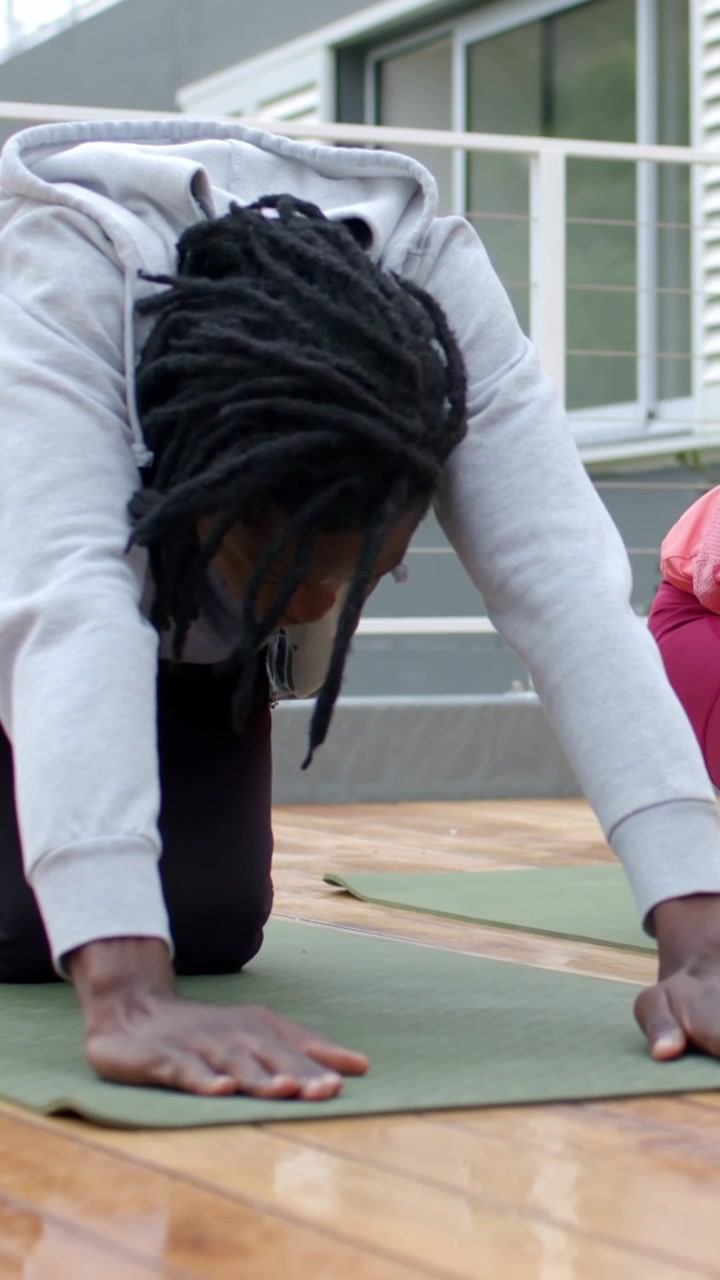 Vertical video: Shifting from knees, man in hoodie lowering torso on green deck mat for stretching