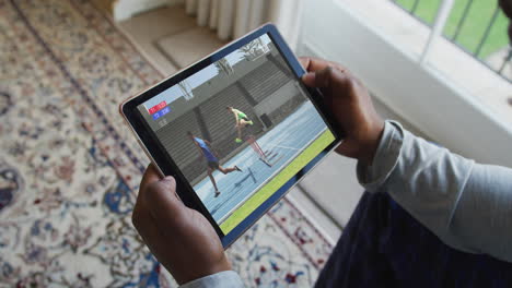 compuesto de un hombre sentado en casa viendo un evento de atletismo en una tableta