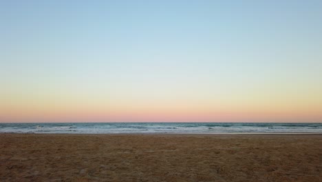 Toma-En-Cámara-Lenta-De-Una-Relajante-Puesta-De-Sol-En-La-Playa-Con-Cielo-Despejado-Y-Colores-Brillantes