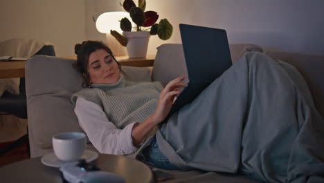 happy model using laptop lying at lamp light zoom on. smiling woman resting