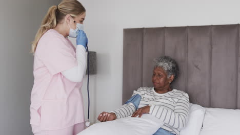 caucasian female nurse in mask checking pressure of senior african american woman, slow motion