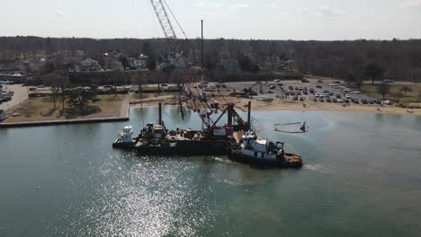 aerial circle panning shot of harbor setting with tugboat and barge with crane attached