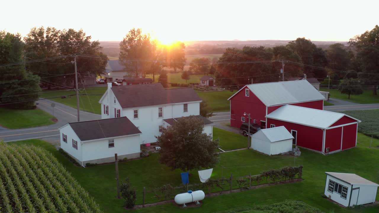 Aerial establishing shot of white house, red barn in rural America, USA at summer sunrise, sunset