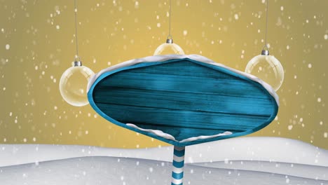 hanging bauble decorations and snow falling over blank blue sign post on winter landscape