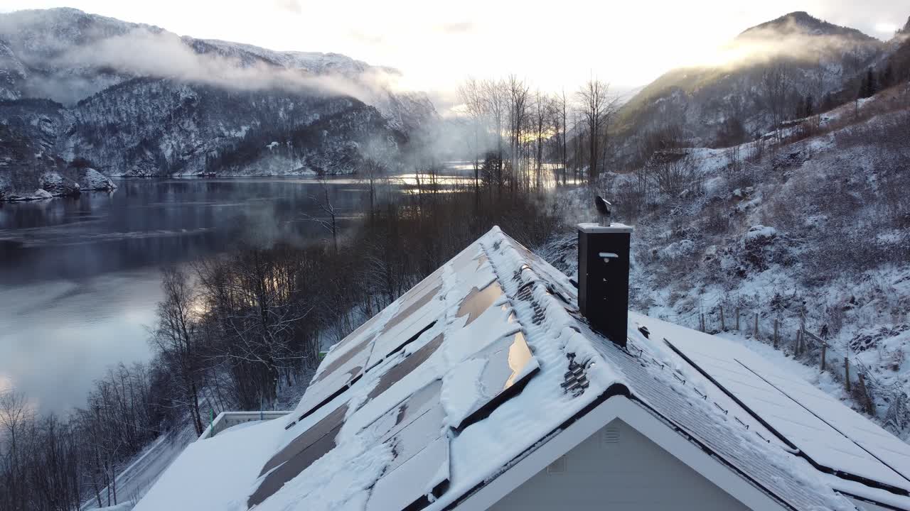 눈 덮힌 태양 지붕 위로 굴뚝 연기를 통해 비행 - 눈 덮힌 풍경과 피요르드 풍경 배경에서 앞으로 움직이는 아침 공중 - 노르웨이