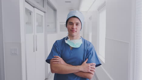 portrait of male surgeon wearing scrubs and mask standing in hospital corridor