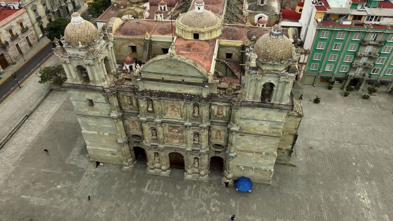 Drone orbit around the front facade of Oaxaca Cathedral Nuestra Señora de la Asunción, showcasing towers, domes, and green cantera stone details