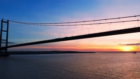 Humber-Bridge-bathed-in-the-warmth-of-sunset,-with-cars-seamlessly-traversing-its-length,-captured-in-a-breathtaking-aerial-view