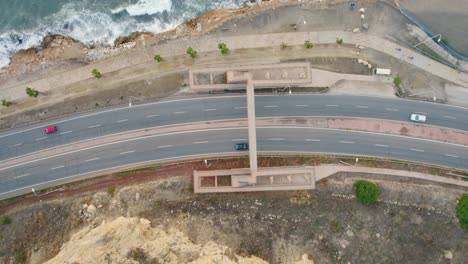 rocket drone shot revealing coastal road and seashore, aiming down to the road, with cars passing by