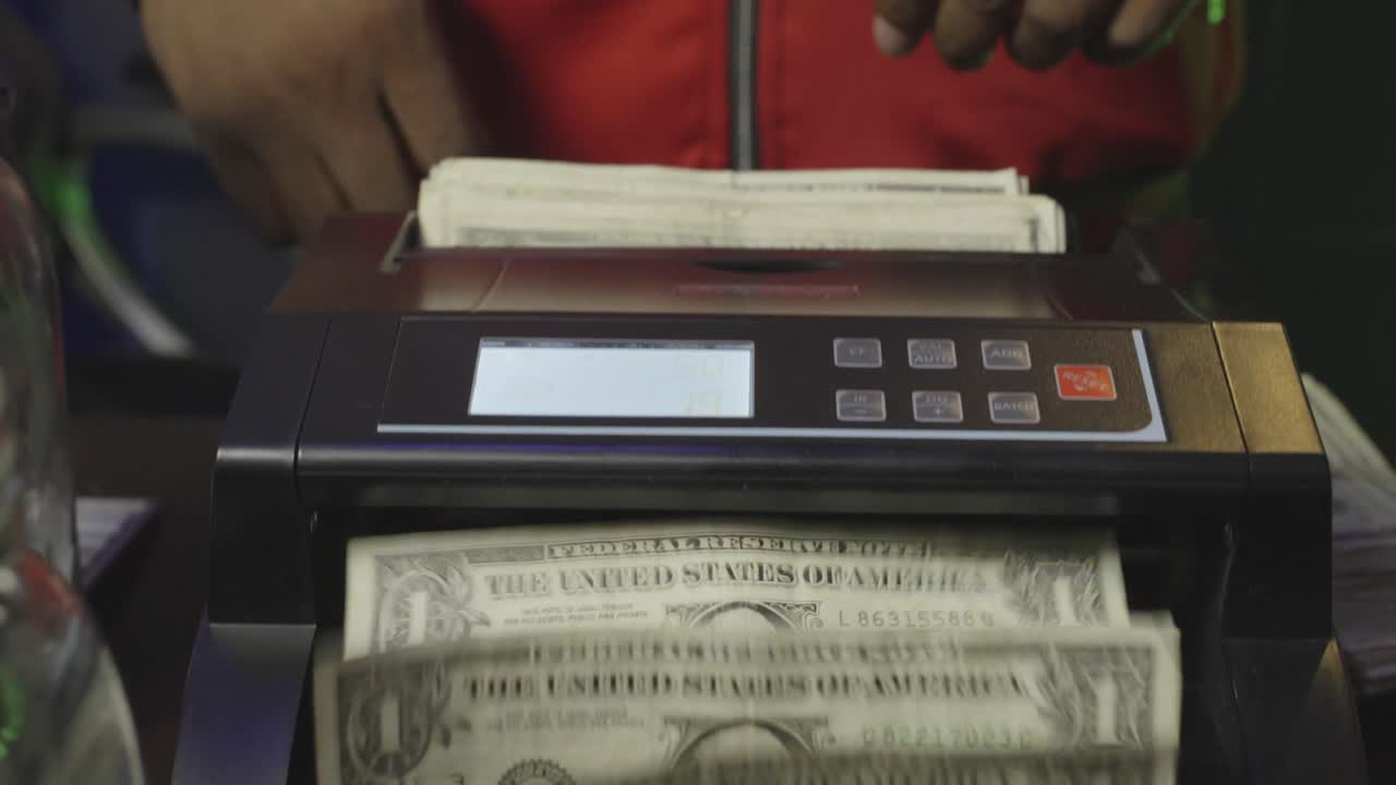 A close-up shot of hands preparing a thick stack of bills for a digital money counter—capturing the flow of street currency and business hustle.