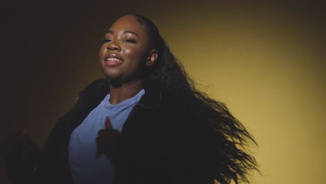 head and shoulders studio portrait shot of young woman dancing in spotlight against yellow background 6