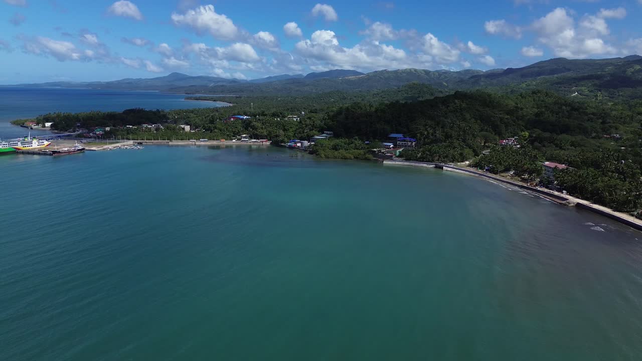 Vista aérea de drone do porto de Odiongan em Romblon, Filipinas, mostrando uma grande balsa de passageiros atracada no porto com a cidade costeira e a orla visíveis sob um céu azul claro em um dia ensolarado.