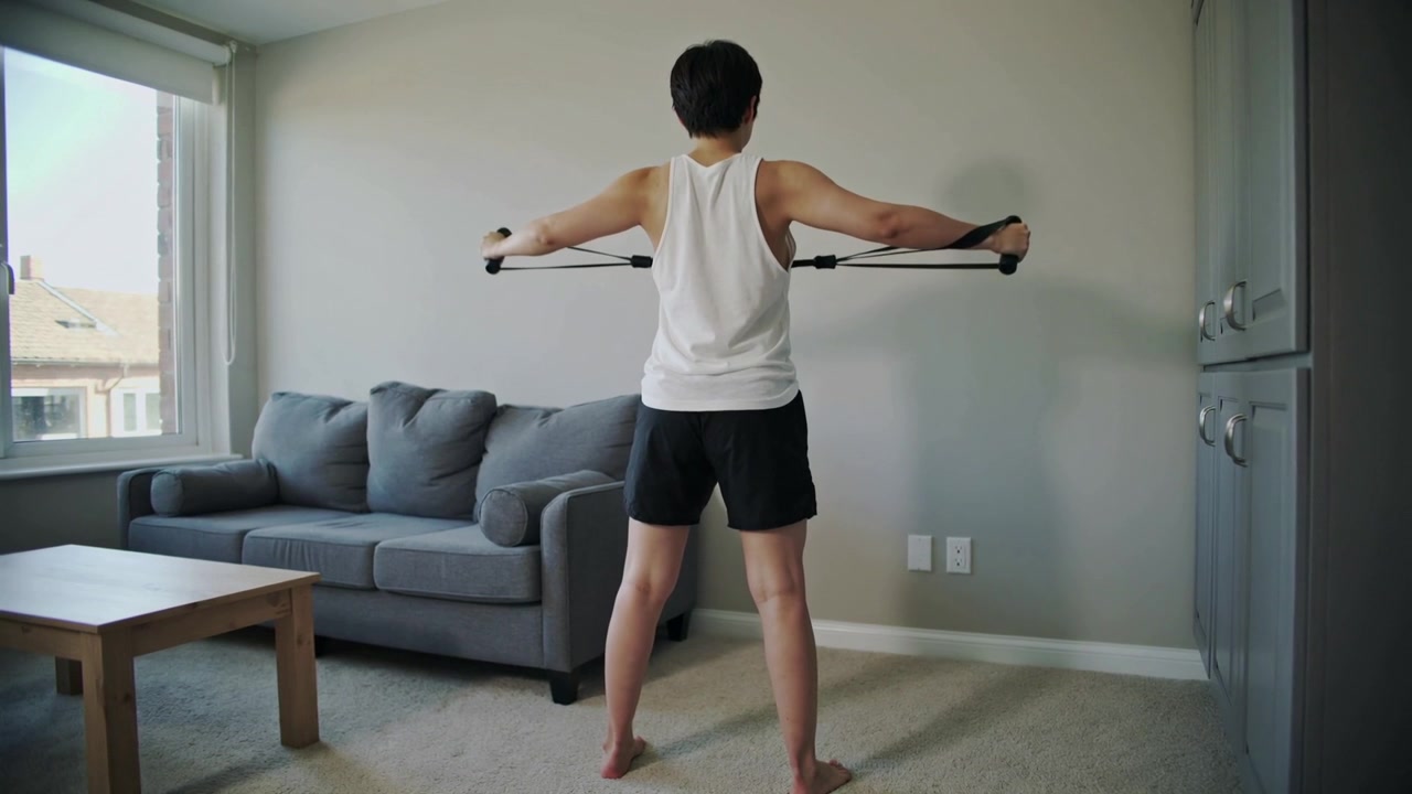 Gripping band handles, man pulling outward at home in white tank and black shorts for strength