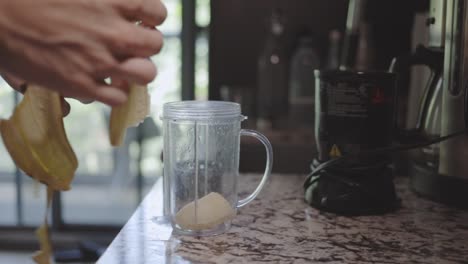 manos poniendo un plátano en una licuadora y preparando un delicioso batido saludable - de cerca