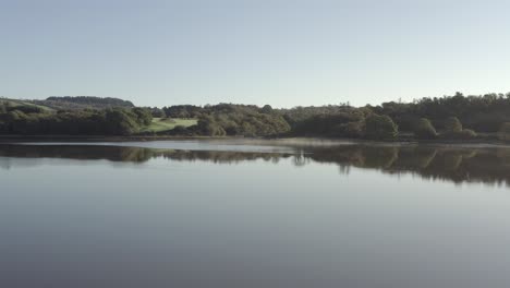 low misty morning aerial over calm river toward green space park