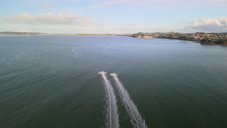 Bei-Sonnenuntergang-Schnell-Hinter-2-Jetskis-Entlang-Der-Küste-Von-Orewa-Beach-In-Neuseeland-Fliegen